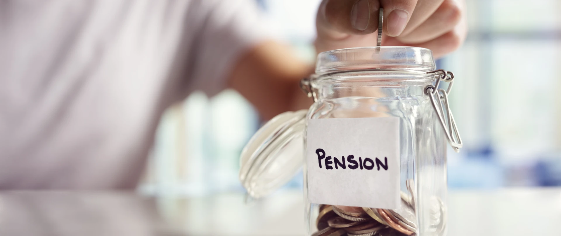 En person putter en mønt i et glas med andre mønter, hvor der står pension på.
