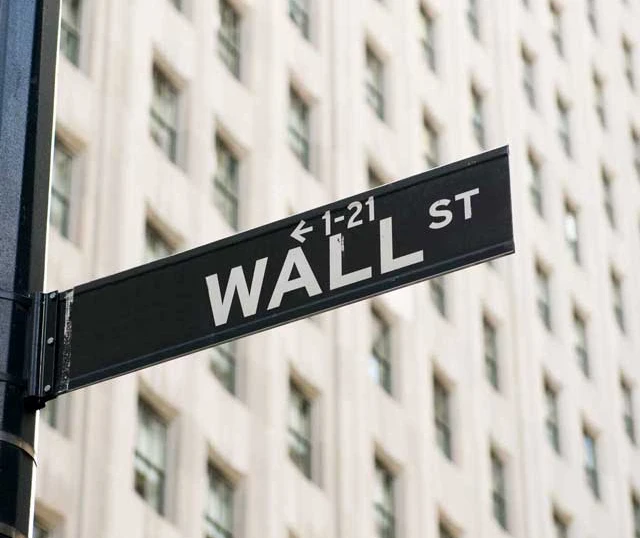 Vejskilt for Wall Street foran en bygning, symboliserer finansverdenens centrum og økonomisk aktivitet.