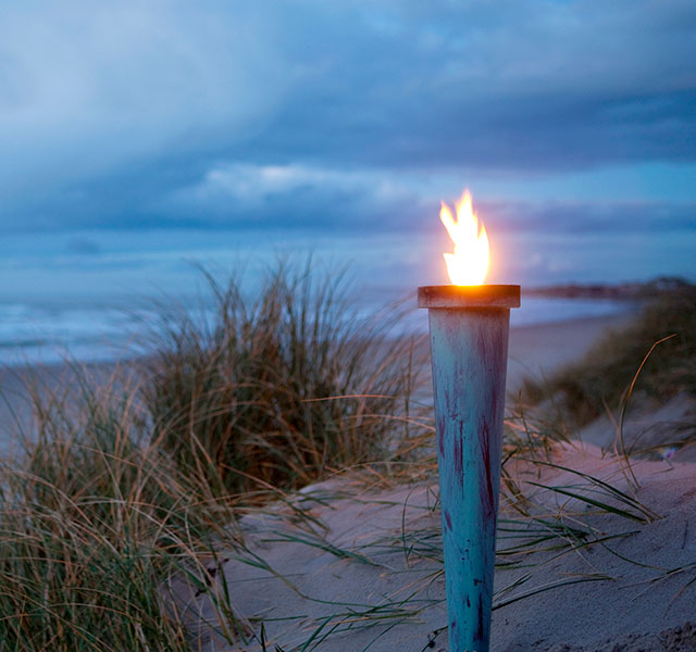 Brændende fakkel på en strand med mørk himmel i baggrunden