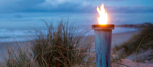 Brændende fakkel på en strand med mørk himmel i baggrunden