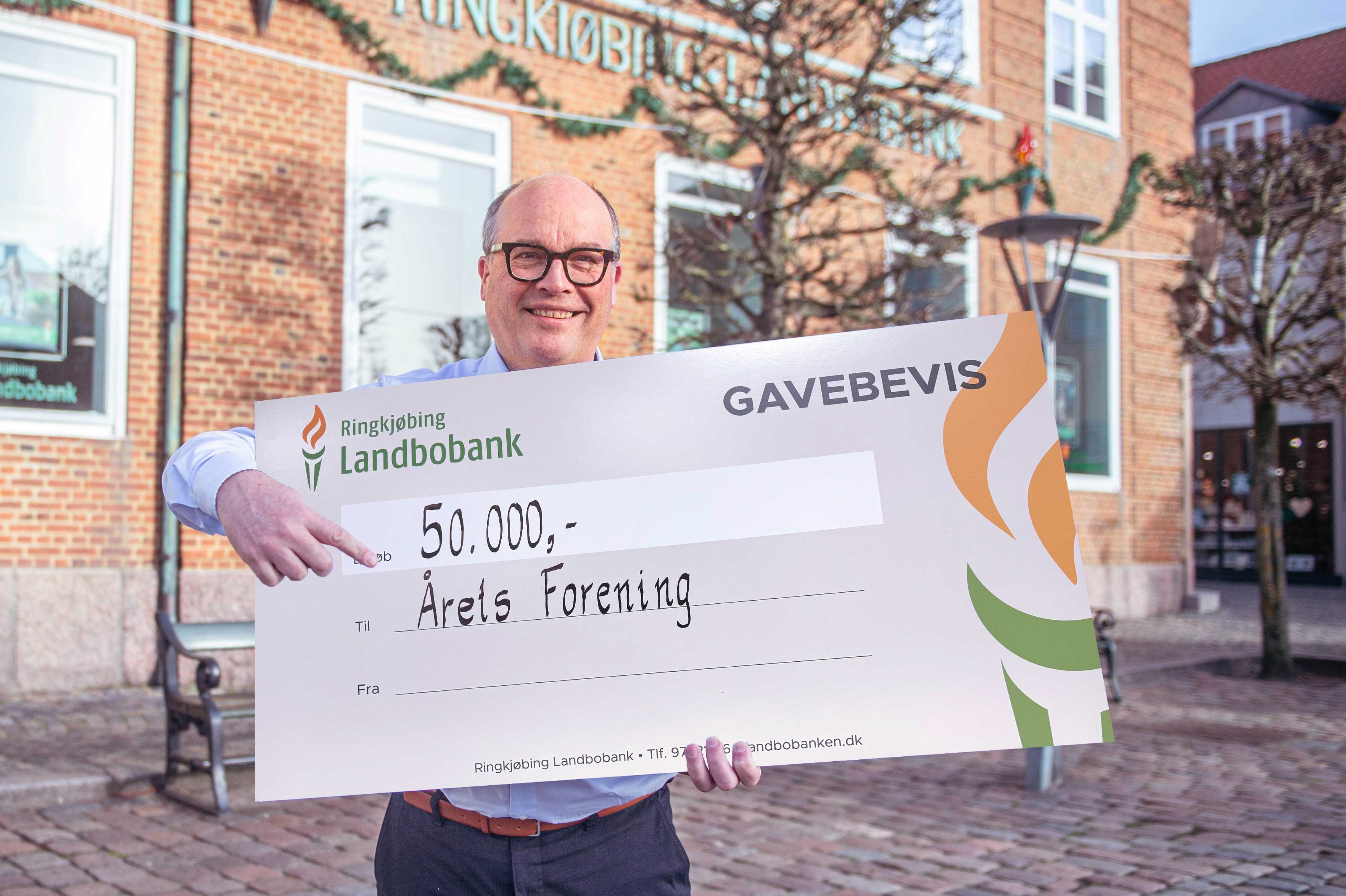 Privatdirektør Lars Knudsen står foran banken med et gavebevis på 33.333 kroner til Årets Forening