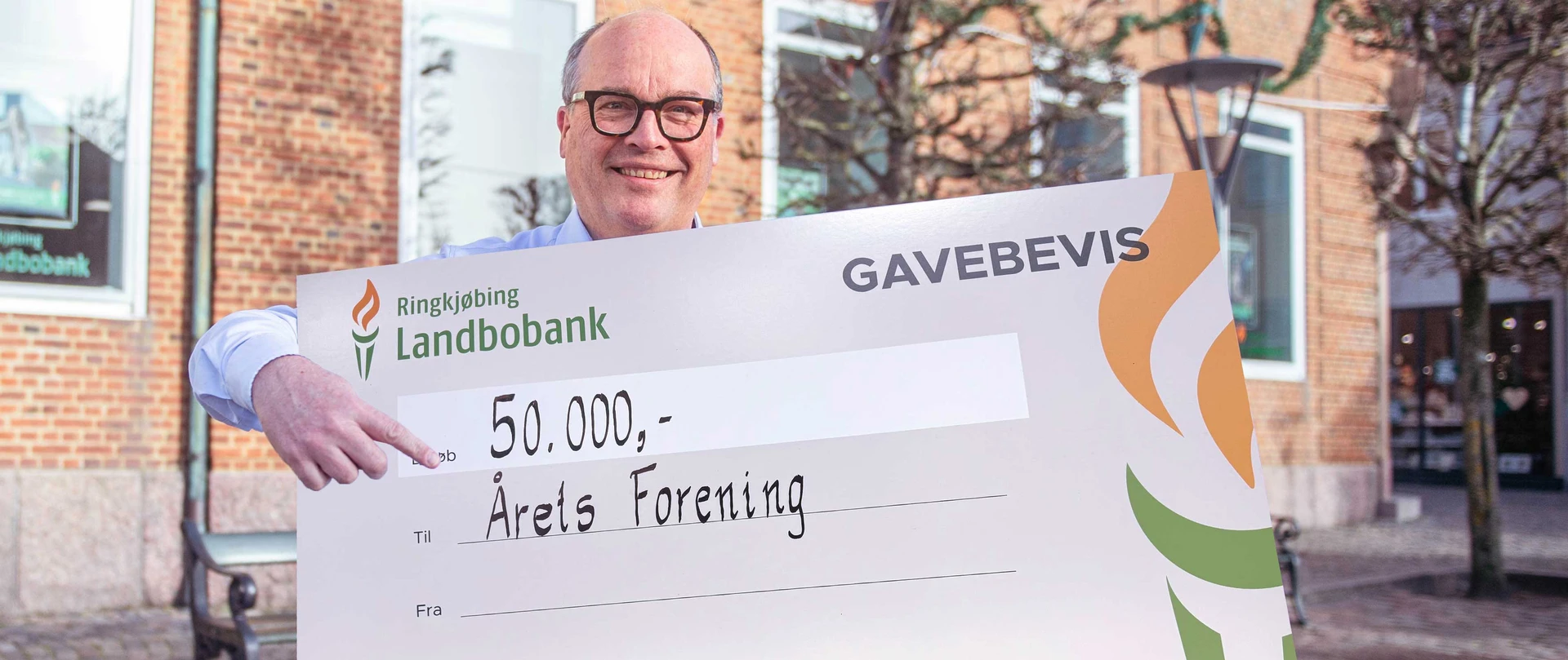 Privatdirektør Lars Knudsen står foran banken med et gavebevis på 33.333 kroner til Årets Forening
